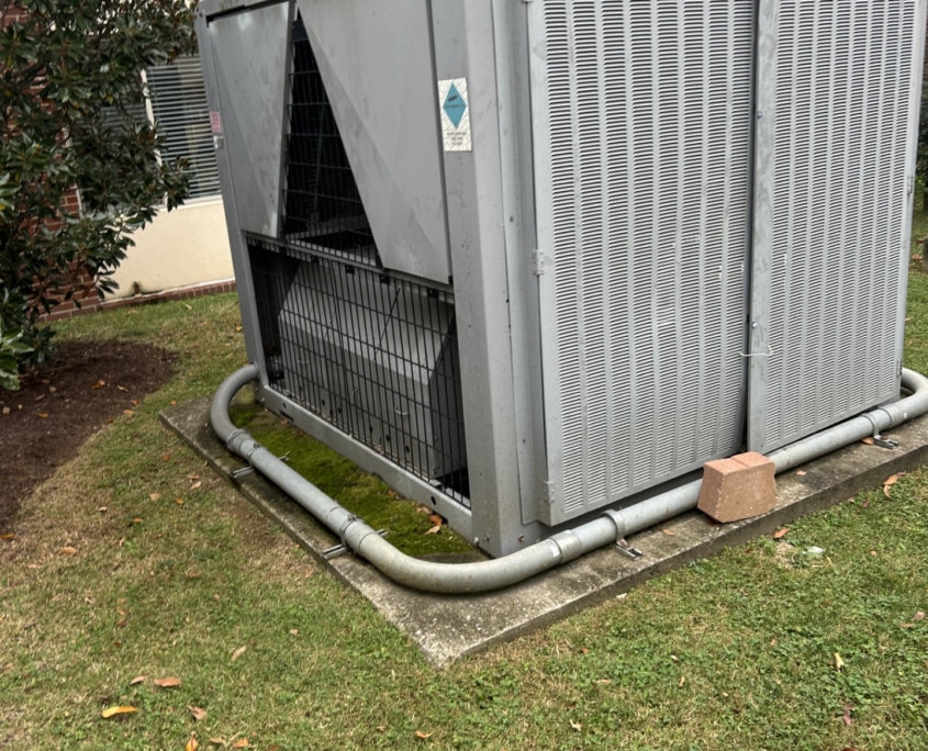 Large industrial air conditioning unit outside a brick building, surrounded by grass and a few fallen leaves.