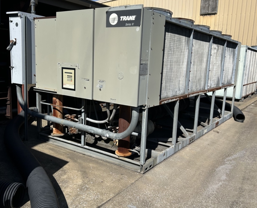 Industrial Trane cooling unit with metal housing, visible pipes, and a clear blue sky in the background.