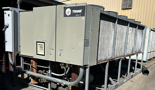 A large Trane Series II cooling unit with multiple condensers, resting on a metal platform in an industrial setting.