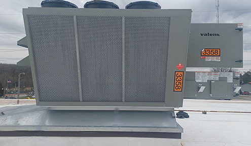 A rooftop HVAC unit with a metal casing and three large fans, labeled "Valent" with the number 3358, set against a cloudy sky.