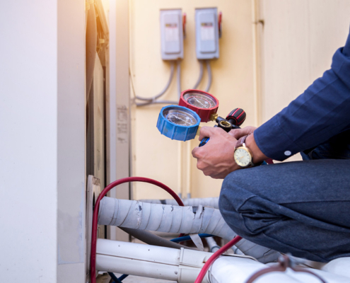 repairs A technician holding blue and red gauges, inspecting HVAC equipment with hoses connected, sunlight illuminating the scene.